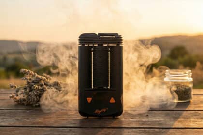 Waporyzator Mighty+ od Storz & Bickel umieszczony na drewnianym stole w ciepłym świetle zachodzącego słońca, otoczony gęstą, aksamitną parą i suszem roślinnym.