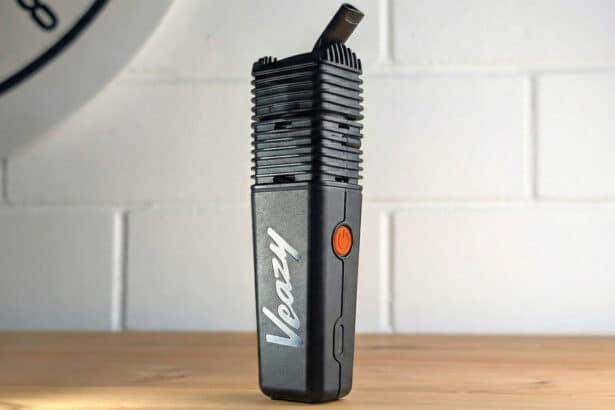 Czarny waporyzator przenośny Storz & Bickel Veazy stojący na drewnianym blacie na tle białej ceglanej ściany – zdjęcie wyróżniające do artykułu "Recenzja Veazy".