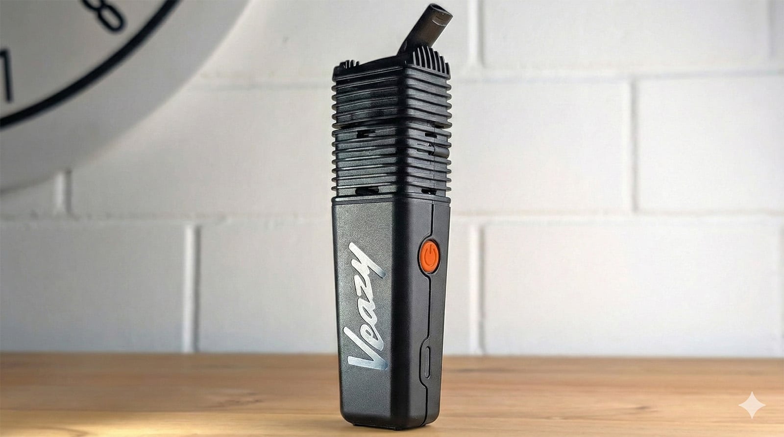Czarny waporyzator przenośny Storz & Bickel Veazy stojący na drewnianym blacie na tle białej ceglanej ściany – zdjęcie wyróżniające do artykułu "Recenzja Veazy".